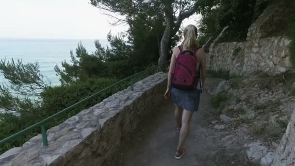 Donna turistica viaggia nel paese mediterraneo durante la stagione primaverile. Ragazza a piedi il sentiero in pietra con il mare su un backgorund — Video Stock