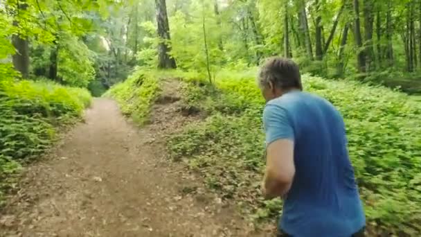 Vuxen man kör jogga utomhus i en skog natur på en skog spår och njuter av det och ser gärna — Stockvideo