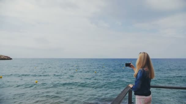 Chica adolescente tomando fotos en la playa. Un disparo de mano. Movimiento lento — Vídeos de Stock