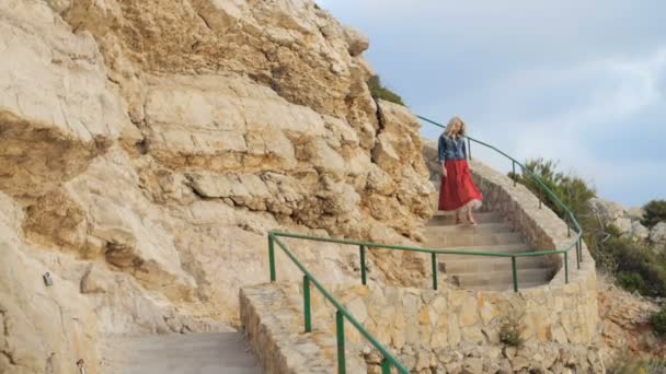 Romantic girl in red skirt walk down the stairs at the coast side — Stock Video