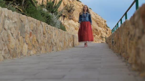 Romantisches Mädchen in rotem Rock geht die Straße entlang an der Küste entlang — Stockvideo