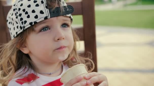 Menina senta-se na cadeira e come sorvete — Vídeo de Stock