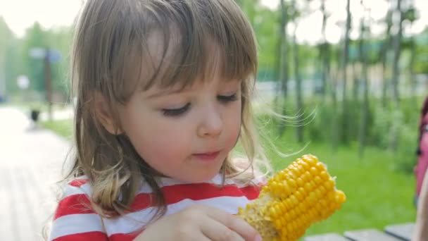 Sunny girl with corn happily eating fruit — Stock Video