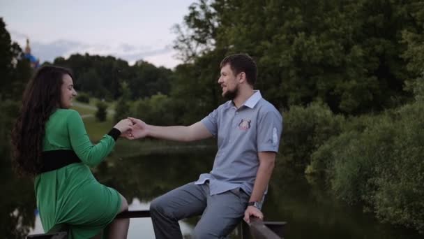 Couple assis et tenir leurs mains près du lac dans le parc — Video