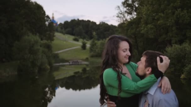 Pareja se sienta y sostiene sus manos cerca del lago en el parque — Vídeos de Stock