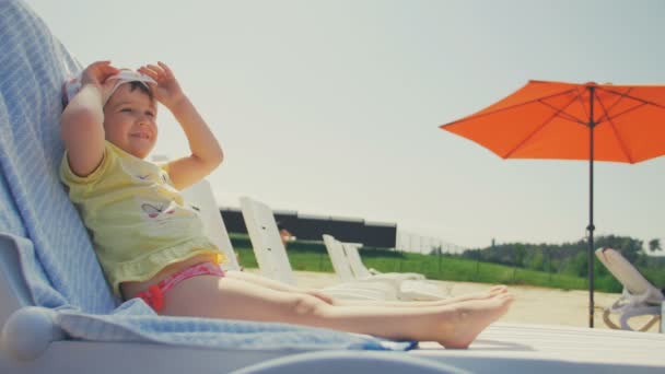 Happy little baby girl take sunbath in chair at beach — Stock Video