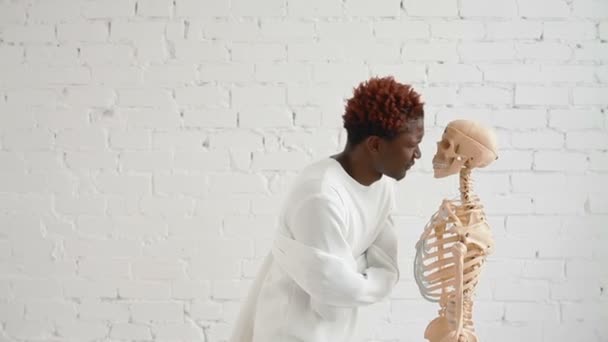 An insane black man wearing a straitjacket dance and looking at human skeleton stand — Stock Video