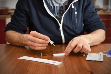 Jaketteki adam evde koronavirüs covid 19 için antikor testi yapıyor. Hızlı bir test kiti açtı ve hızlı antijen testinin üzerine bir damla analiz çözeltisi düşürdü.