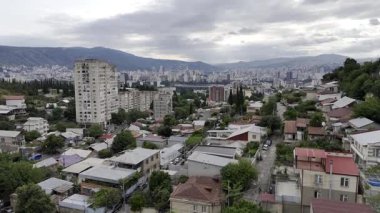 Ön planda yemyeşil çimenlerle çevrili yüksek binalar ve arka planda bir şehir manzarası