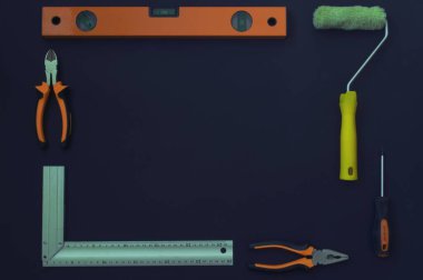 İnşaat aletleri çerçevesi. İnşaat aracı dikdörtgen bir çerçeve içinde serilmiştir. Siyah arka plan. İnşaat seviyesi, pense, boya silindiri, tornavida.