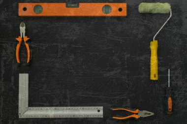 İnşaat aletleri çerçevesi. İnşaat aracı dikdörtgen bir çerçeve içinde serilmiştir. Siyah arka plan. Çizik bir fotoğrafın etkisi. İnşaat seviyesi, pense, boya silindiri, tornavida.