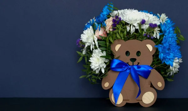 Çiçekli tahta ayı, tatil için hediye buketi. Mavi ve beyaz kasımpatılar mavi arkaplanda.