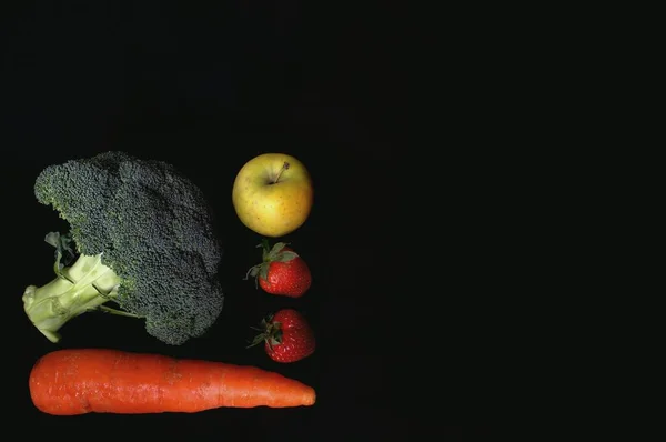 Sağlıklı beslenme. Siyah arka planda havuç, brokoli, elma ve çilek.