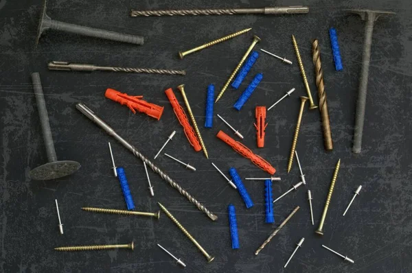 Vidalar, cıvatalar ve matkaplar masanın üzerine saçılmış. Kahverengi arka planda inşaat malzemeleri. Çizilmiş fotoğraf efekti