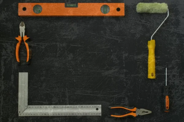 İnşaat aletleri çerçevesi. İnşaat aracı dikdörtgen bir çerçeve içinde serilmiştir. Siyah arka plan. Çizik bir fotoğrafın etkisi. İnşaat seviyesi, pense, boya silindiri, tornavida.