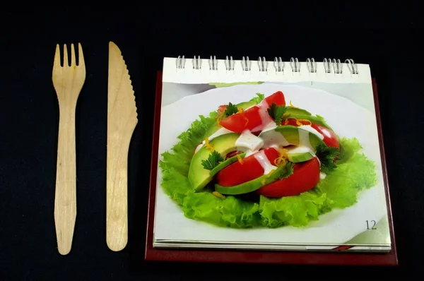 Menünün yanında tahta bir çatal ve bıçak, yemek tarifi kitabı. Siyah bir arkaplanda