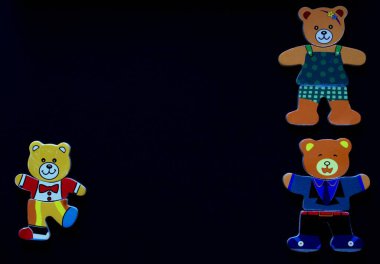 Siyah arka planda üç renkli ayının çocuk figürleri. Ayı anne, baba ve ayı yavrusu. Farklı köşelerde duruyorlar.