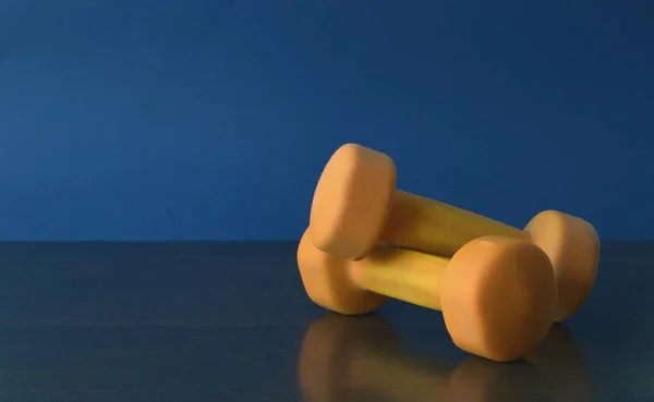 İki turuncu halter mavi bir arka planda masanın üzerinde yatıyor. Spor ve aktif yaşam tarzı. Fotoğrafın kenarındaki dambıllar.