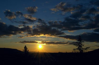 Dağlarda gün batımı. Gün batımının tüm renkleri. Bulutlu mavi gökyüzü. Turuncu gün batımı