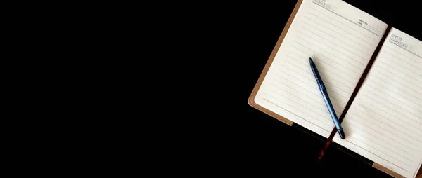 Siyah arka planda bir kalemle yazmak için bir defter. Pankart
