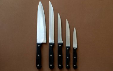 Farklı boyutlarda mutfak bıçakları kahverengi arka planda sıralanır.
