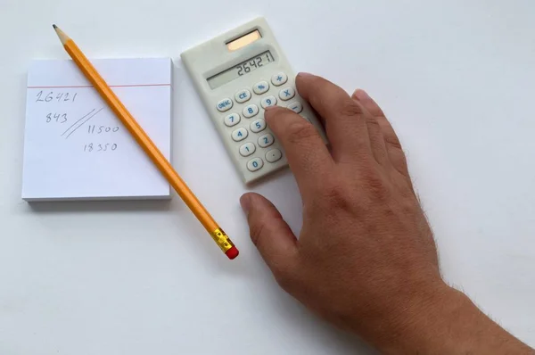Notlar için bir sayfa, hesaplamalar kurşun kalemle yazılır. Hesaplamalar bir hesap makinesinde yapılır. Beyaz arka plan ve insan eli