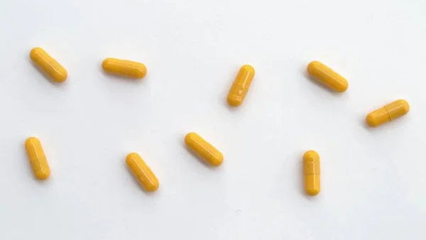 黄色の錠剤カプセルは白い背景に散在しています — ストック写真