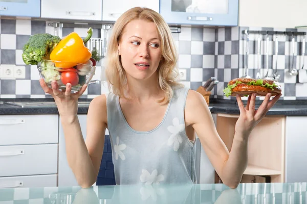 Mulher escolhendo entre legumes e sanduíche — Fotografia de Stock