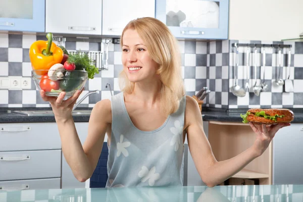 Woman choosing between vegetables and sandwich — Stock Photo, Image