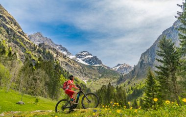 pretty senior woman riding her electric mountain bike the Oy Tal Valley near Oberstdorf, Allgau Alps, Bavaria, Germany clipart