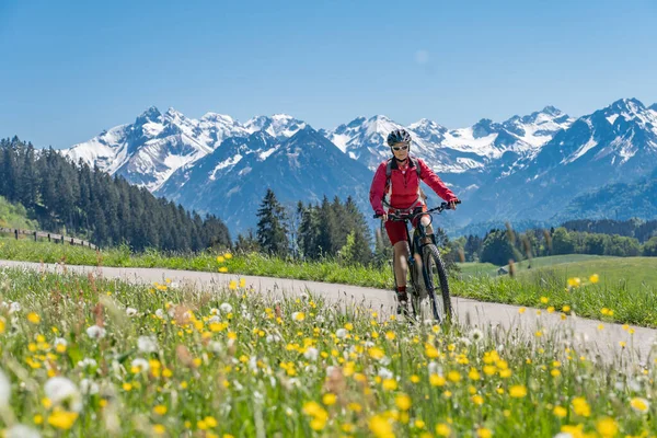 Oberstdorf yakınlarındaki İller Vadisi 'nde, arka planda Allgau Yüksek Alpleri, Allgau Alpleri, Bavyera, Allgau Alpleri ile birlikte bisiklete binen son sınıf güzeli bir kadın., 