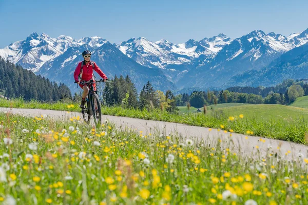 Oberstdorf yakınlarındaki İller Vadisi 'nde, arka planda Allgau Yüksek Alpleri, Allgau Alpleri, Bavyera, Allgau Alpleri ile birlikte bisiklete binen son sınıf güzeli bir kadın., 