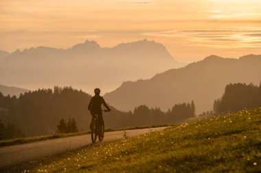 Aktif bir kadın gün batımında elektrikli dağ bisikletini sürüyor Saentis Dağı 'nın muhteşem siluetinin önünde, Appenzell Switthe