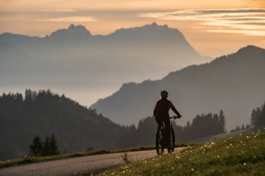 Aktif bir kadın gün batımında elektrikli dağ bisikletini sürüyor Saentis Dağı 'nın muhteşem siluetinin önünde, Appenzell Switthe