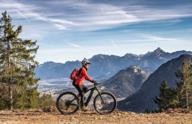 Doğu Allgaeu dağlarında elektrikli dağ bisikletine binen son sınıf güzel bir kadın ve arka planda Zugspitze Dağı, Bavyera, Almanya