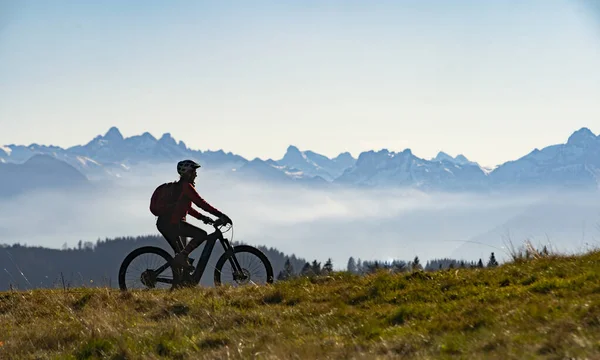 woman on electric mountain bike as silhouette in front of the mountain chain of the Allgaeu High Alps near Oberstdorf, Bavaria, Germany