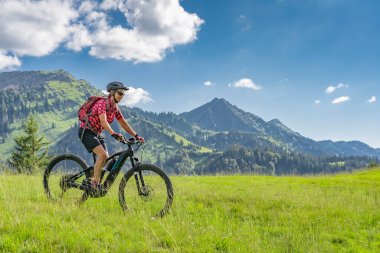 Almanya 'da Immenstadt, Algu, Bavyera yakınlarındaki Allgau Alplerinde elektrikli dağ bisikleti süren aktif son sınıf öğrencisi bir kadın.