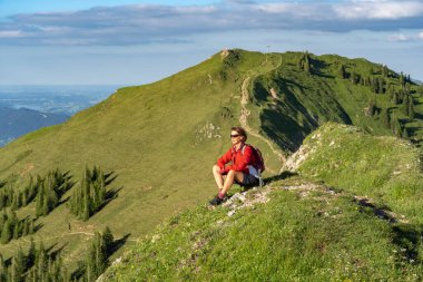 Almanya 'nın Bavyera, Immenstadt yakınlarındaki Allgau Alpleri' ndeki Nagelfluh zincirinin tepesinde sıcak şafak ışığında yürüyüş yaparken dinlenen yaşlı güzel bir kadın.