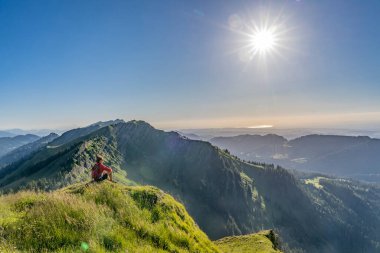 Almanya 'nın Bavyera, Immenstadt yakınlarındaki Allgau Alpleri' ndeki Nagelfluh zincirinin tepesinde sıcak şafak ışığında yürüyüş yaparken dinlenen yaşlı güzel bir kadın.