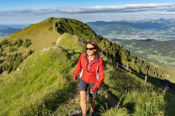 active senior woman mountain running in the early evening in warm dawn light on the ridge of the Nagelfluh chain in the Allgau Alps near Immenstadt, Bavaria, Germany