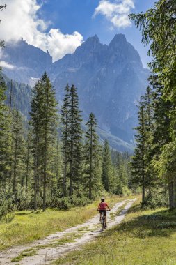 Arka planda Sexten Dolomites nükteli Fischlein Vadisi 'nde bisiklete binen son sınıf güzel bir kadın, Tre cime Ulusal Parkı, Güney Tirol, İtalya 
