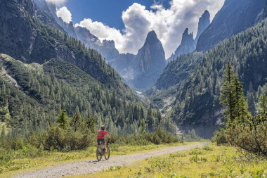 Arka planda Sexten Dolomites nükteli Fischlein Vadisi 'nde bisiklete binen son sınıf güzel bir kadın, Tre cime Ulusal Parkı, Güney Tirol, İtalya 