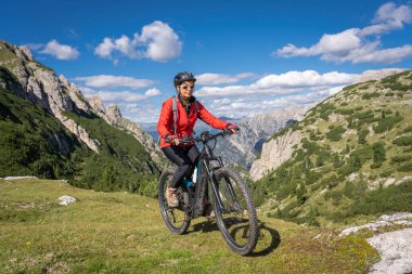 nice and active senior woman riding her electric mountain bike on the high plateau of Pratto Piazzo in the three peaks Dolomites , rocky silhouette of Mount Cristallo in background, South Tirol, Italy clipart