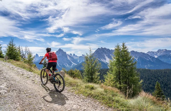 nice and active senior woman riding her electric mountain bike on a old military road from Toblach upt to the summit of Marchkinkele with spectacular view to the Three peaks of Lavaredo, South Tirol,