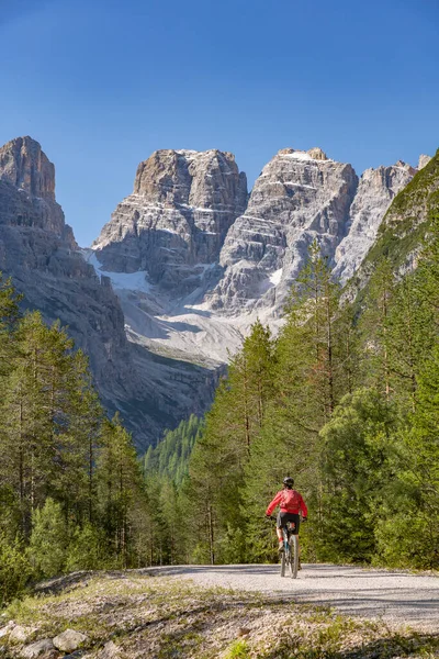 nice and active senior woman riding her electric mountain bike on an old railway embankment in the Hoehlenstein valley  between Toblach and Cortina Dampezzo, Three Peaks Dolomites, South Tirol, Italy