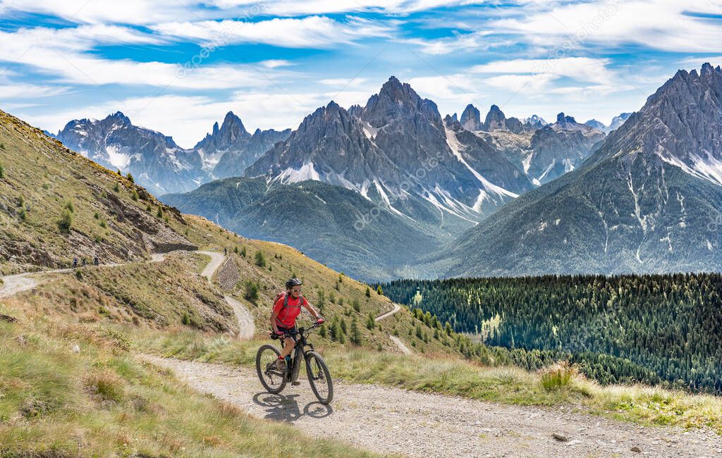 nice and active senior woman riding her electric mountain bike on a old military road from Toblach upt to the summit of Marchkinkele with spectacular view to the Three peaks of Lavaredo, South Tirol, Italy