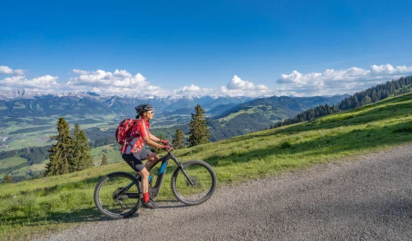 Iller Vadisi 'nin yukarısındaki Sonthofen ve Oberstdorf, Allgau Alps, Bavyera Almanya arasındaki dağlarda elektrikli dağ bisikletine binen son sınıf güzeli bir kadın.