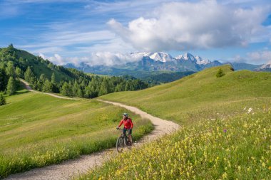 Alta Badia Dolomitleri 'ndeki Pralongia Platosu' nda elektrikli dağ bisikleti süren oldukça aktif yaşlı bir kadın. Arka plan, Güney Tirol ve Trentino, İtalya 'da Marmolata zirvesi buzullarıyla dolu.