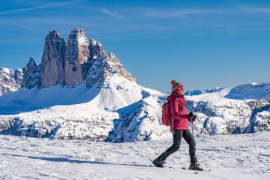 Prato Piazzo 'dan Monte Specie' ye kadar uzanan ünlü Three Peaks 'in altında kar ayakkabısı giyen orta yaşlı güzel bir kadın. Arka planda üç tepesi olan Innichen köyü yakınlarındaki üç meşe Dolomite bölgesinde. Güney Tyrol, İtalya.