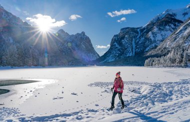 nice active woman snowshoeing on a cold winter morning on the shore of Lago Dobbiaco, Three Peak Dolomites, South Tyrol, Italy clipart